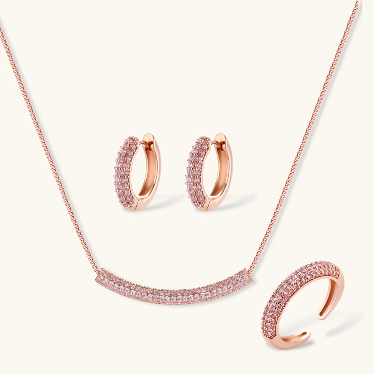 Rose gold pavé zirconia bar necklace, hoop earrings, and open ring set with pink stones on cream background.