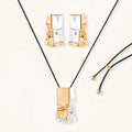 Modern jewelry set with abstract gold and silver pendant on black cord necklace plus matching geometric earrings on white background.