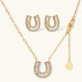 Gold-plated horseshoe necklace and earring set with baguette and round crystals arranged in geometric pattern on white background.