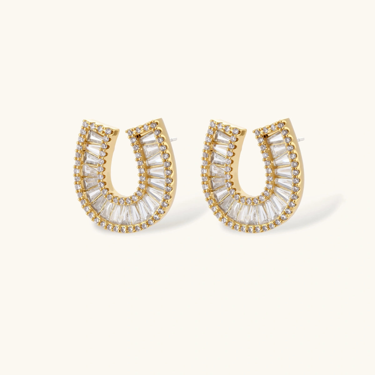 Gold-plated horseshoe necklace and earring set with baguette and round crystals arranged in geometric pattern on white background.